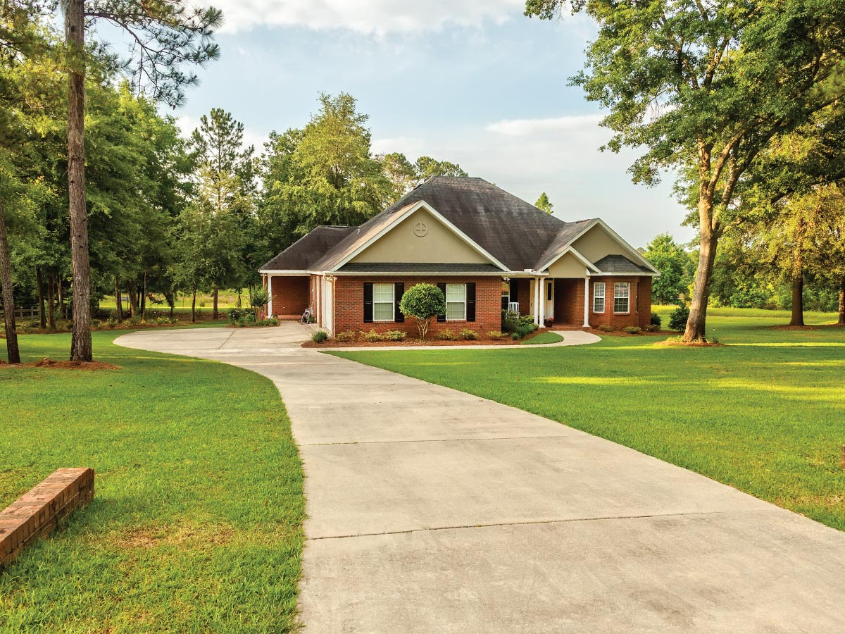 Large house on acreage with long driveway and trees.